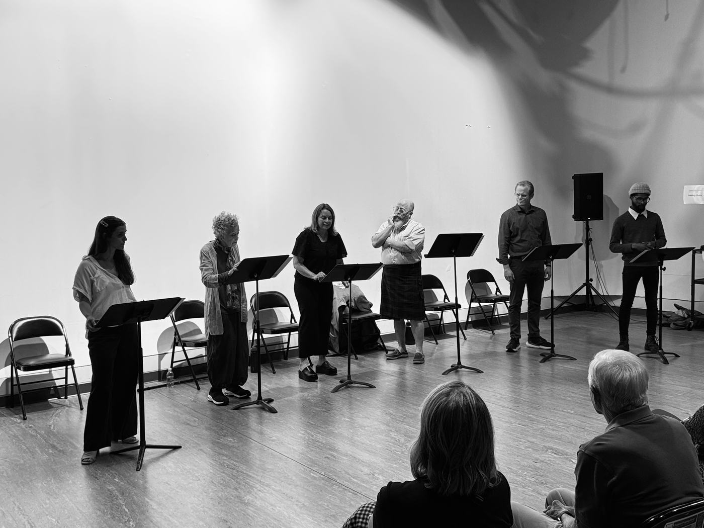 Incline company members performing a staged reading at music stands before a seated audience