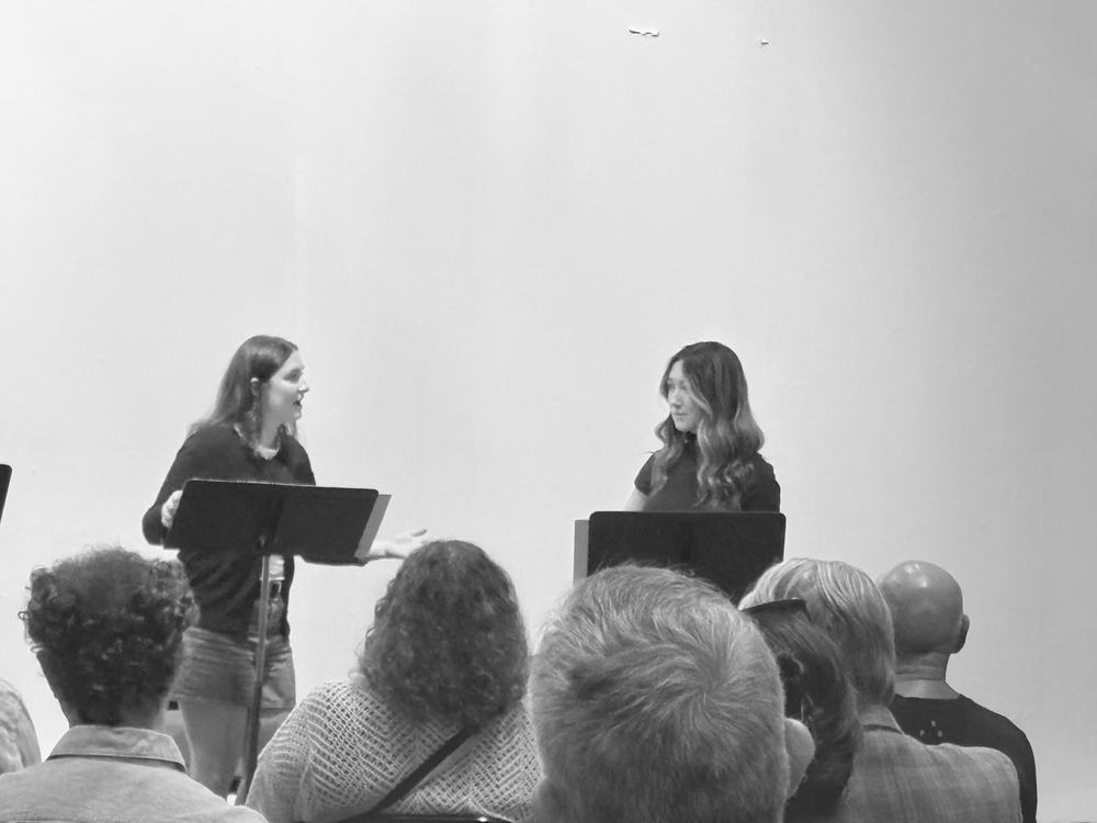 Two actors in dialogue, seen over the heads of the audience