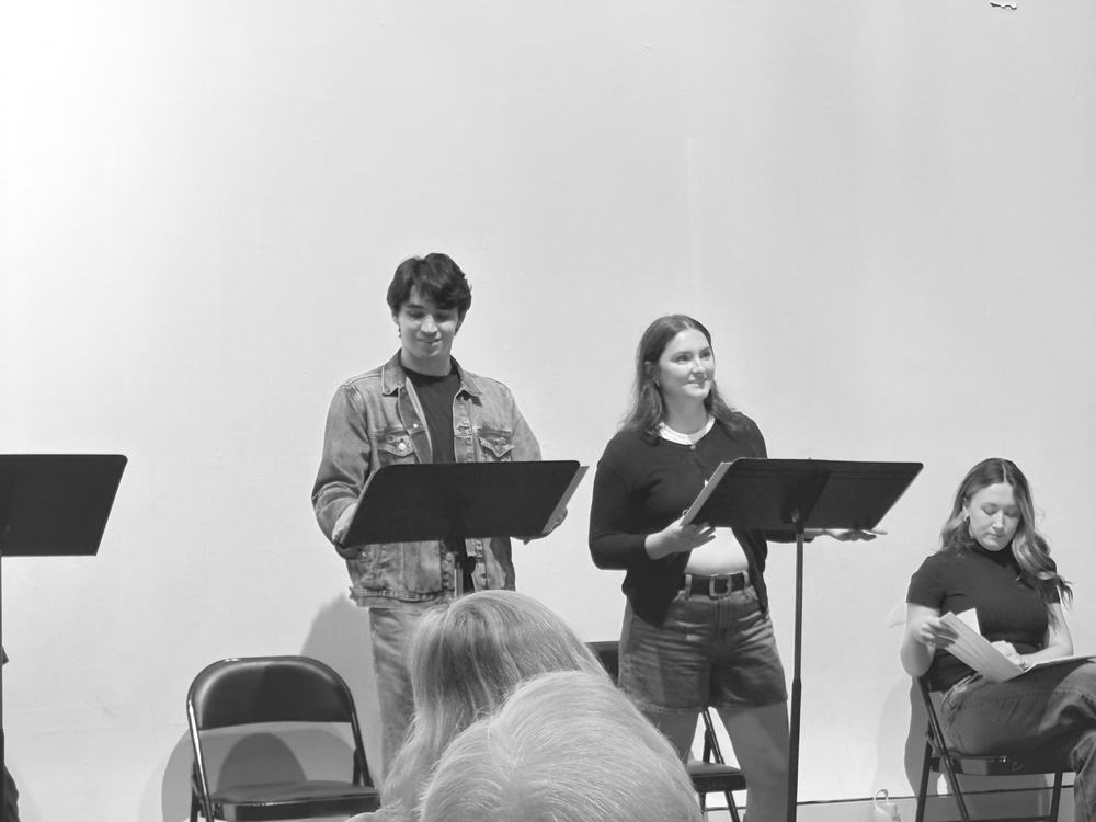 Two actors reading a scene at music stands while a third follows along